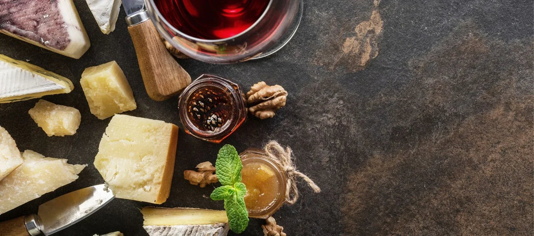 Artisan cheese assortment with honey, nuts, and a glass of red wine on a dark stone surface, ideal for cheesemonger displays and seasonal cheese counter inspiration.