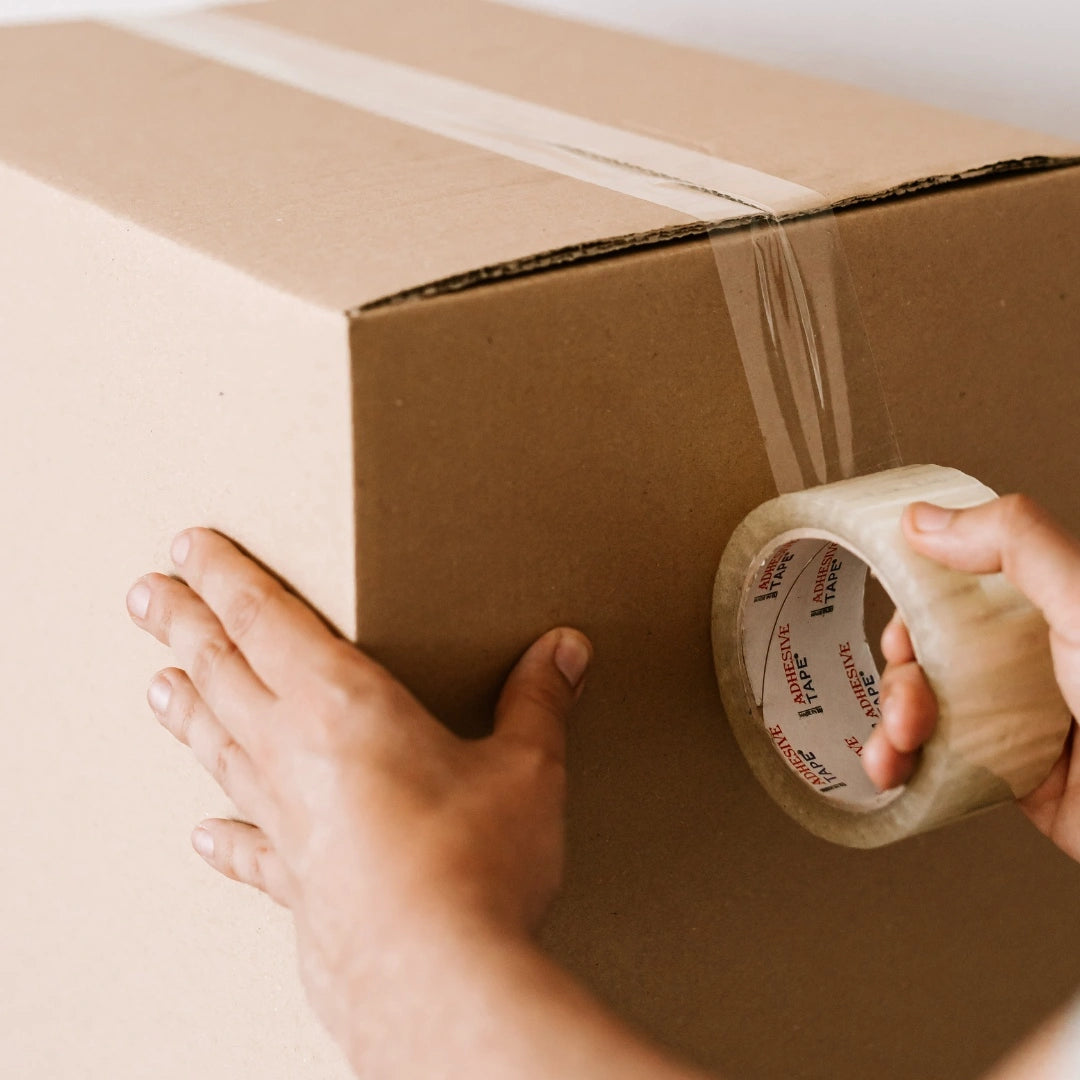 Hands sealing a cardboard shipping box with tape, representing packaging and distribution