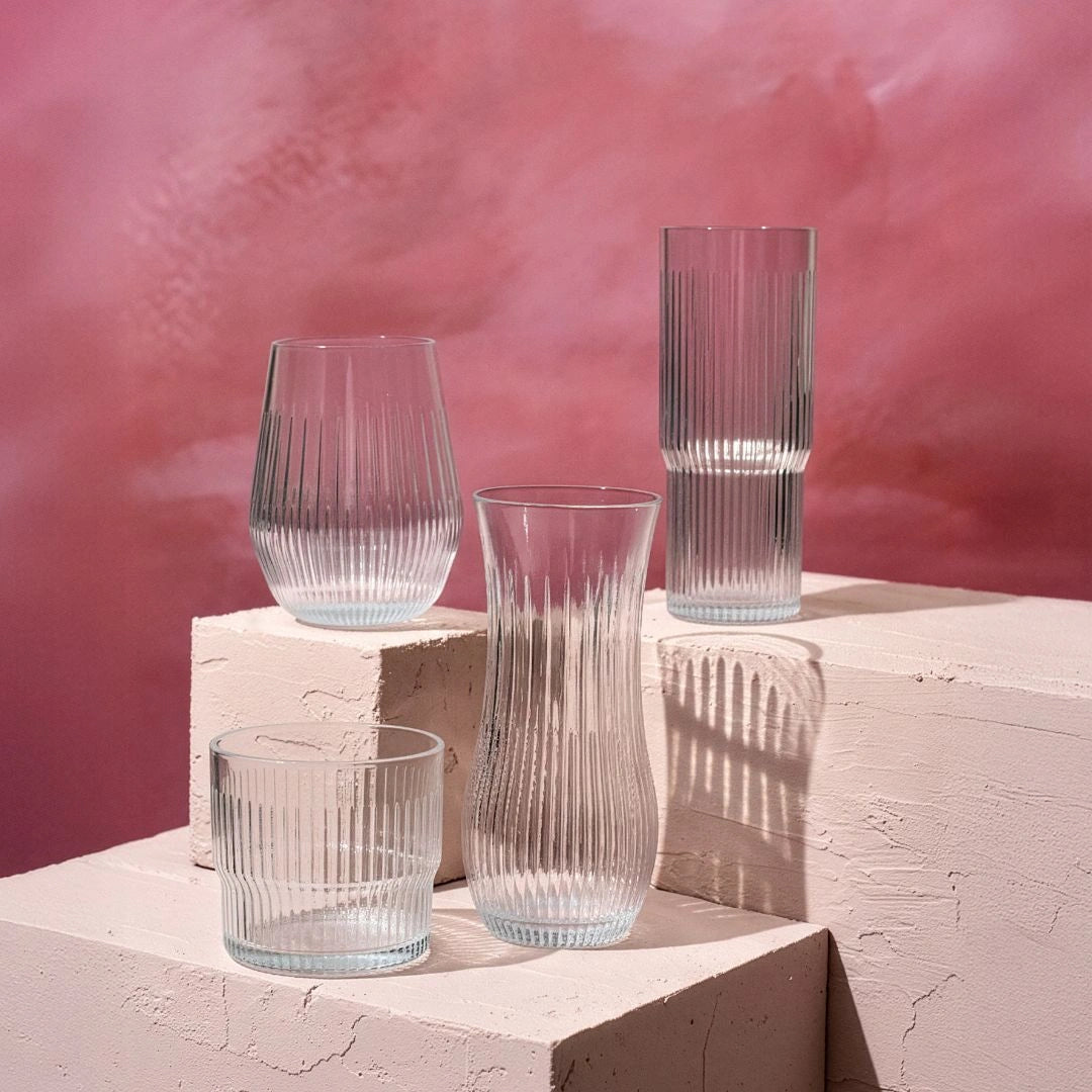 Set of clear Tritan Renew Drinkware on a textured surface with a pink background