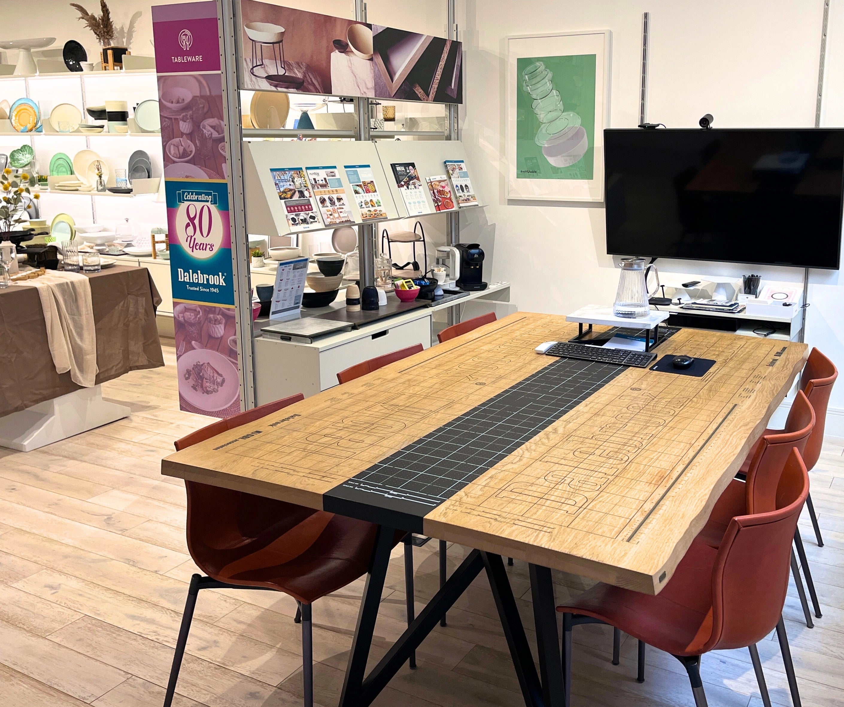 Modern office space with a long wooden table and red chairs, featuring a TV and various decor items for bespoke consultations