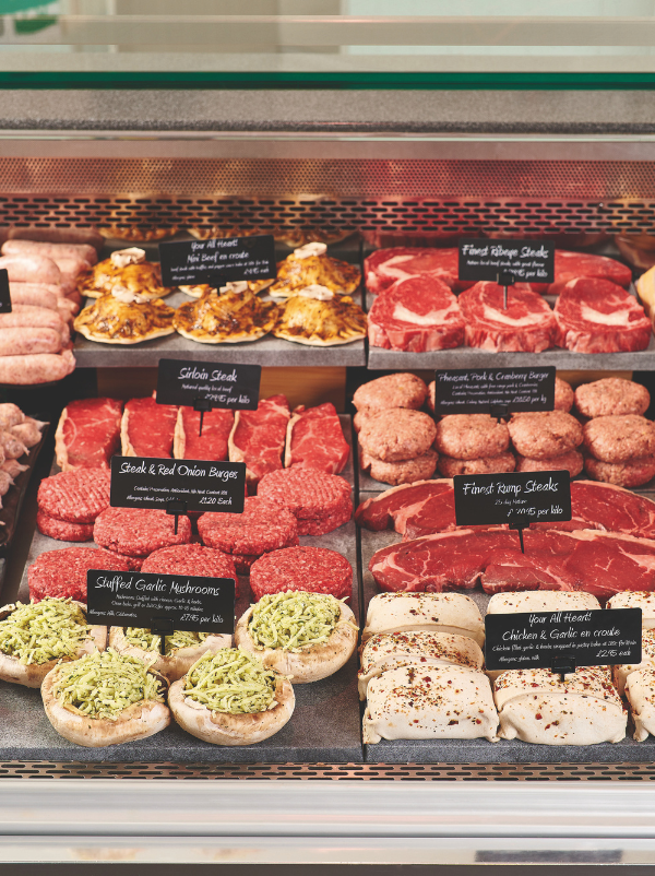 A food display case filled with raw meats, prepared mushrooms, and baked chicken pieces, each labeled with handwritten price tags.