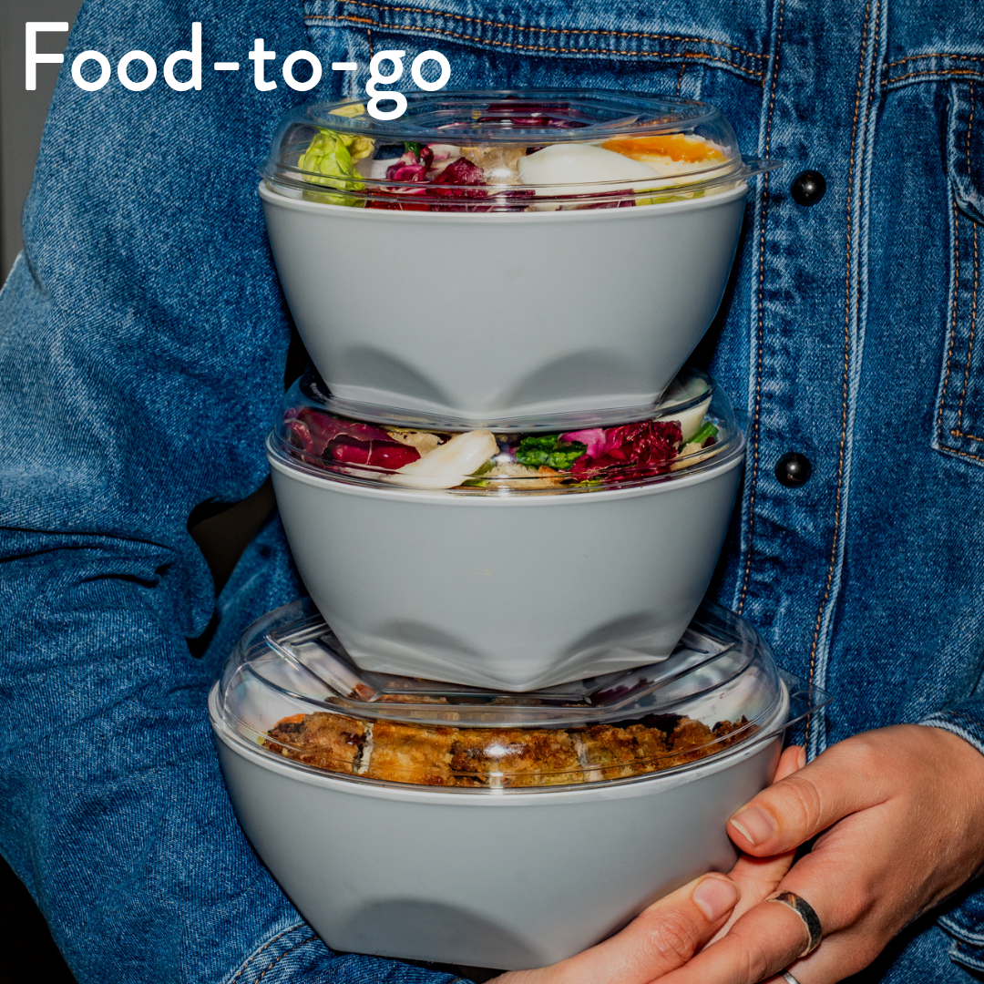 Three stacked light gray food storage containers with clear lids, filled with prepared meals, held by a person wearing a blue denim jacket. The text 'Food-to-go' appears in the top left corner.