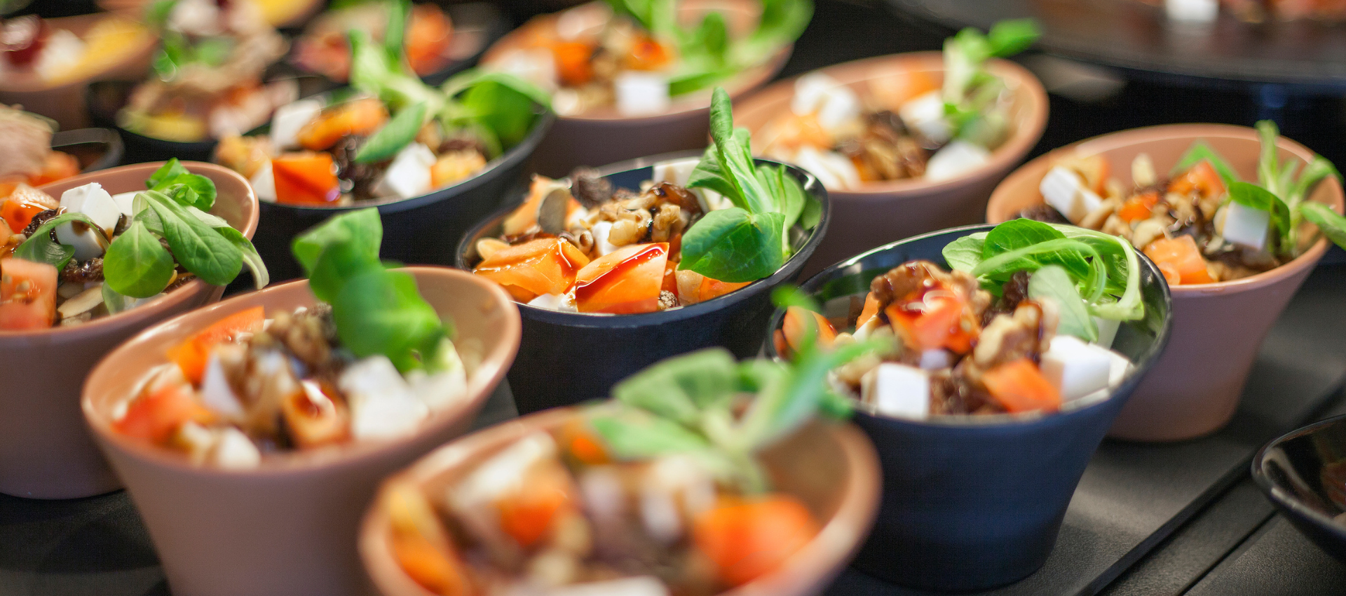 Several small bowls filled with a colorful salad or soup, arranged closely together on a dark surface. The bowls are in soft focus, with the front center bowl slightly sharper.