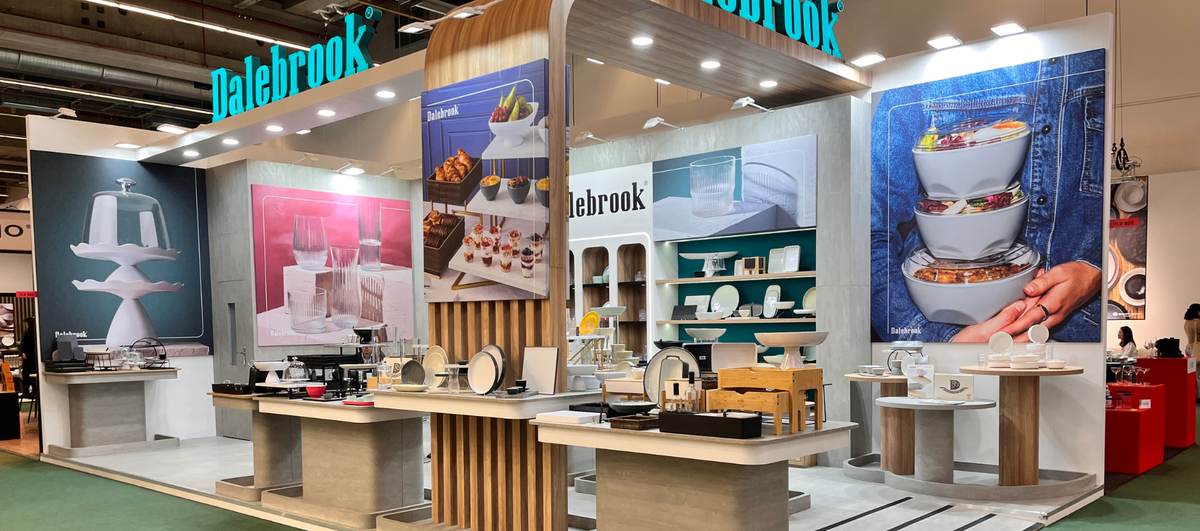 A large Dalebrook kitchen display booth at an exhibition, showcasing various ceramic and glass cookware items, serving ware, and kitchen accessories arranged on tables with large product posters on the walls.