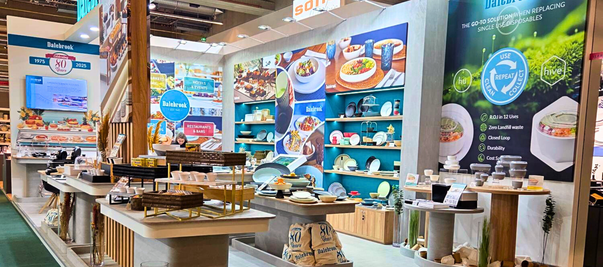 A wide interior view of Dalebrook's retail display or exhibition booth with multiple product tables, shelves, and large promotional posters. The scene includes kitchenware and food-related items, with visible signage and a busy commercial environment.