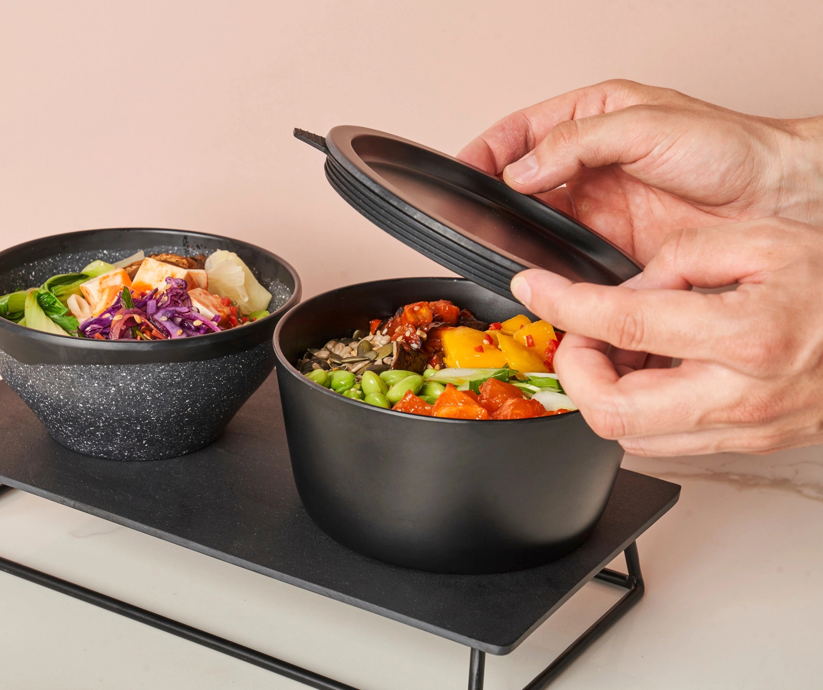 Person opening a black lunch container with food on a light background